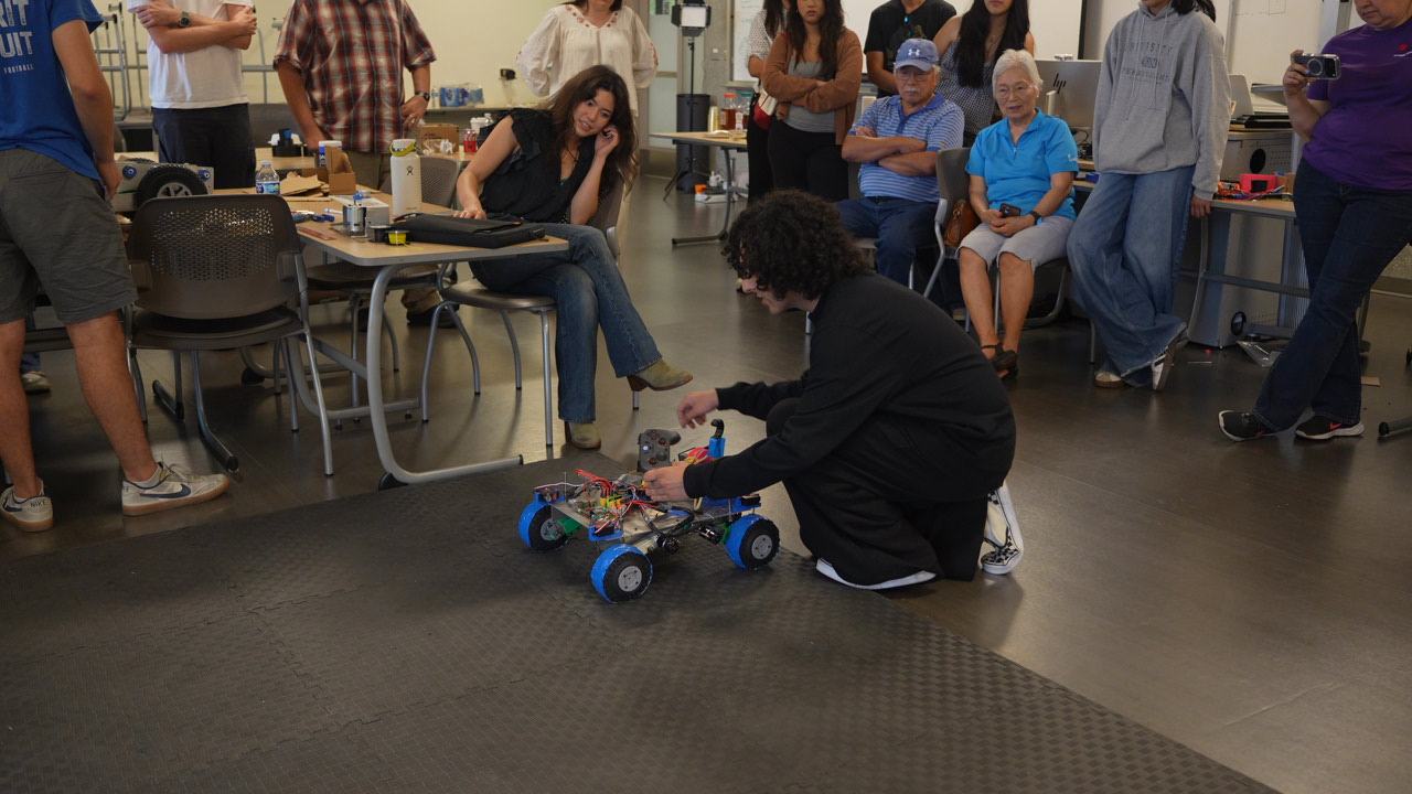 A student setting a robot on the course as the cohort and families watch