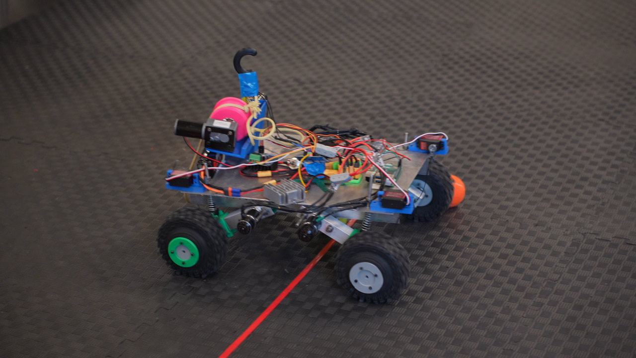 A student-built robot with bright wiring and green wheels on the course