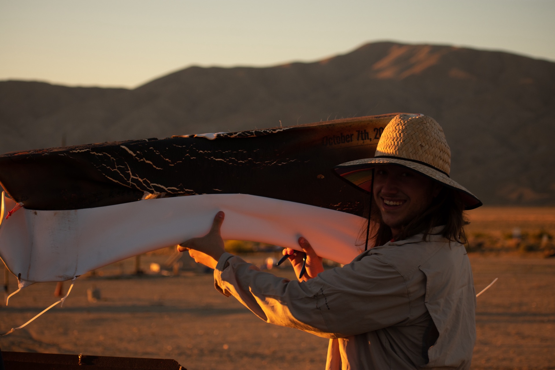 Student holding a rocket fin in the desert at sunset, smiling
