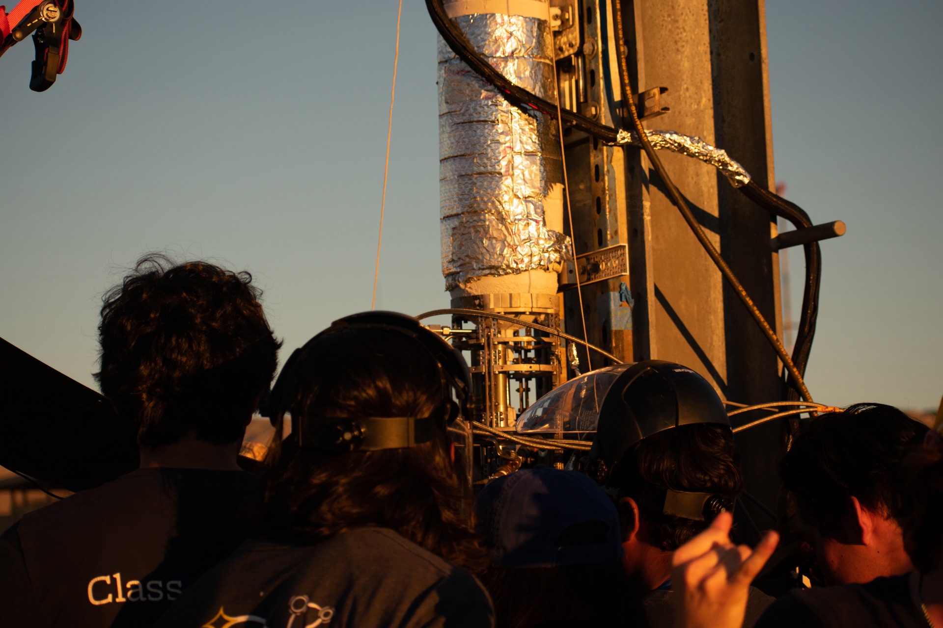 Students in headphones gathered around the rocket on the launch pad at golden hour